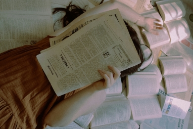 Naisoletettu henkilö lukee sanomalehteä kirjakasan keskellä
