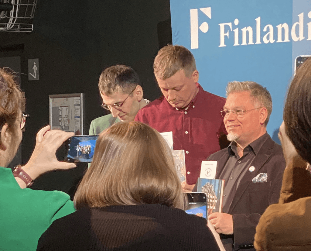 Finlandia-ehdokkaita kuvausseinää vasten ja edessä innokkaita kuvaajia.